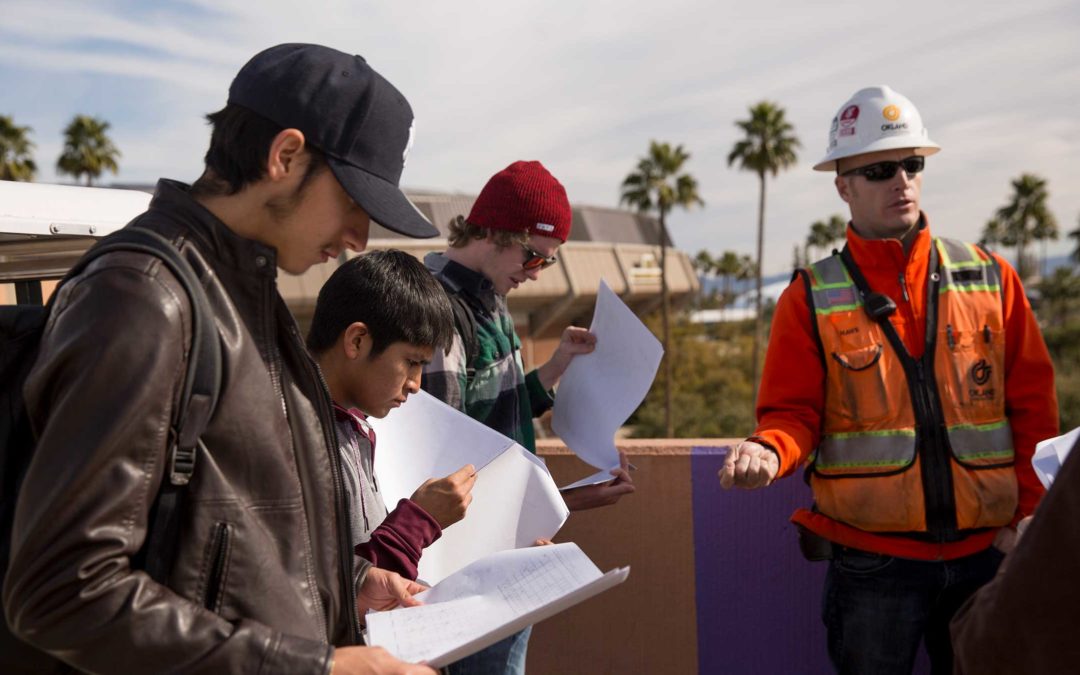 A group of students stand with their professor in class at a construction site.