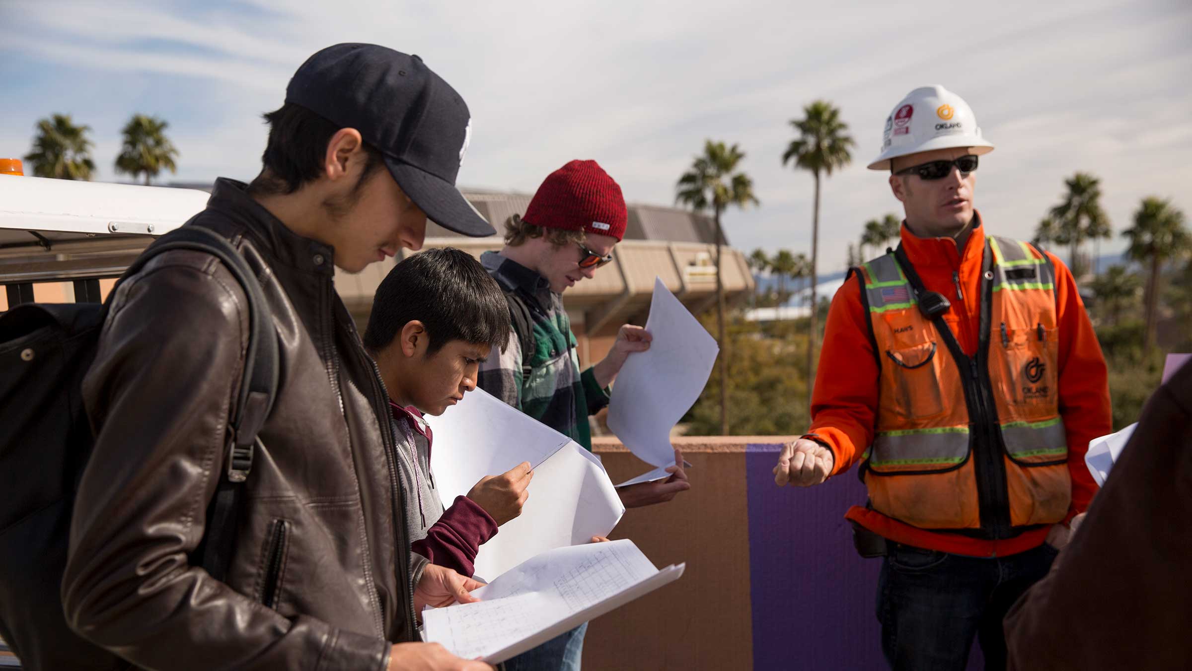 A group of students stand with their professor in class at a construction site.